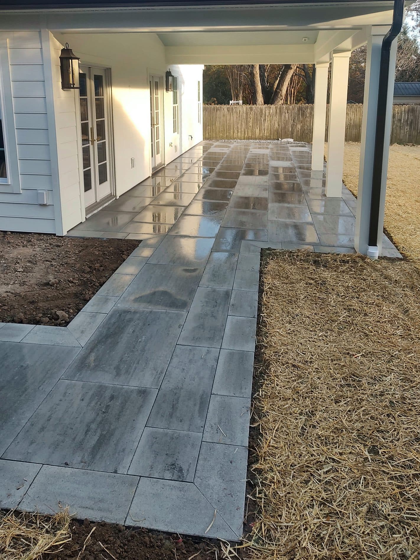 Large-format gray pavers running from a covered porch into a walkway, freshly rinsed, with straw over new seed.