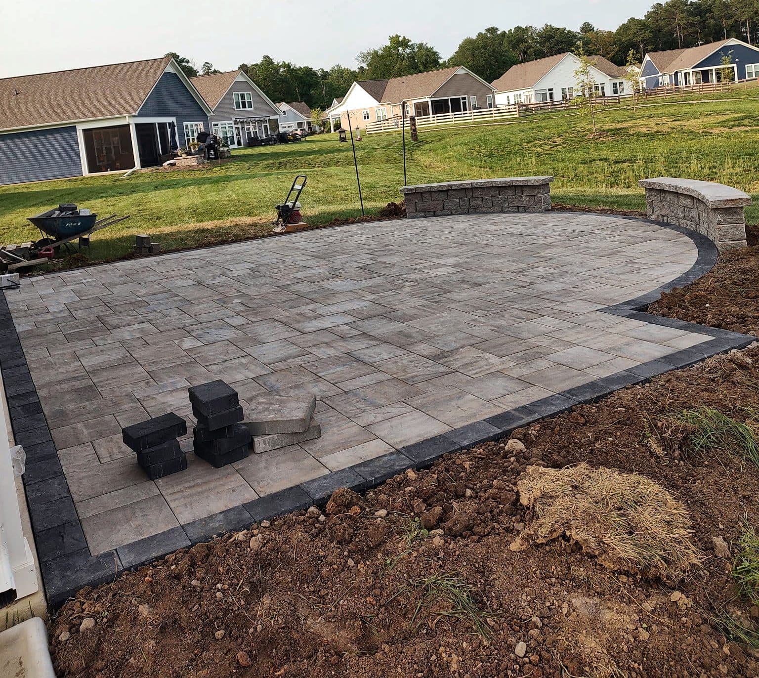 Paver patio with a charcoal border and two seat walls nearing completion, with materials still on site.