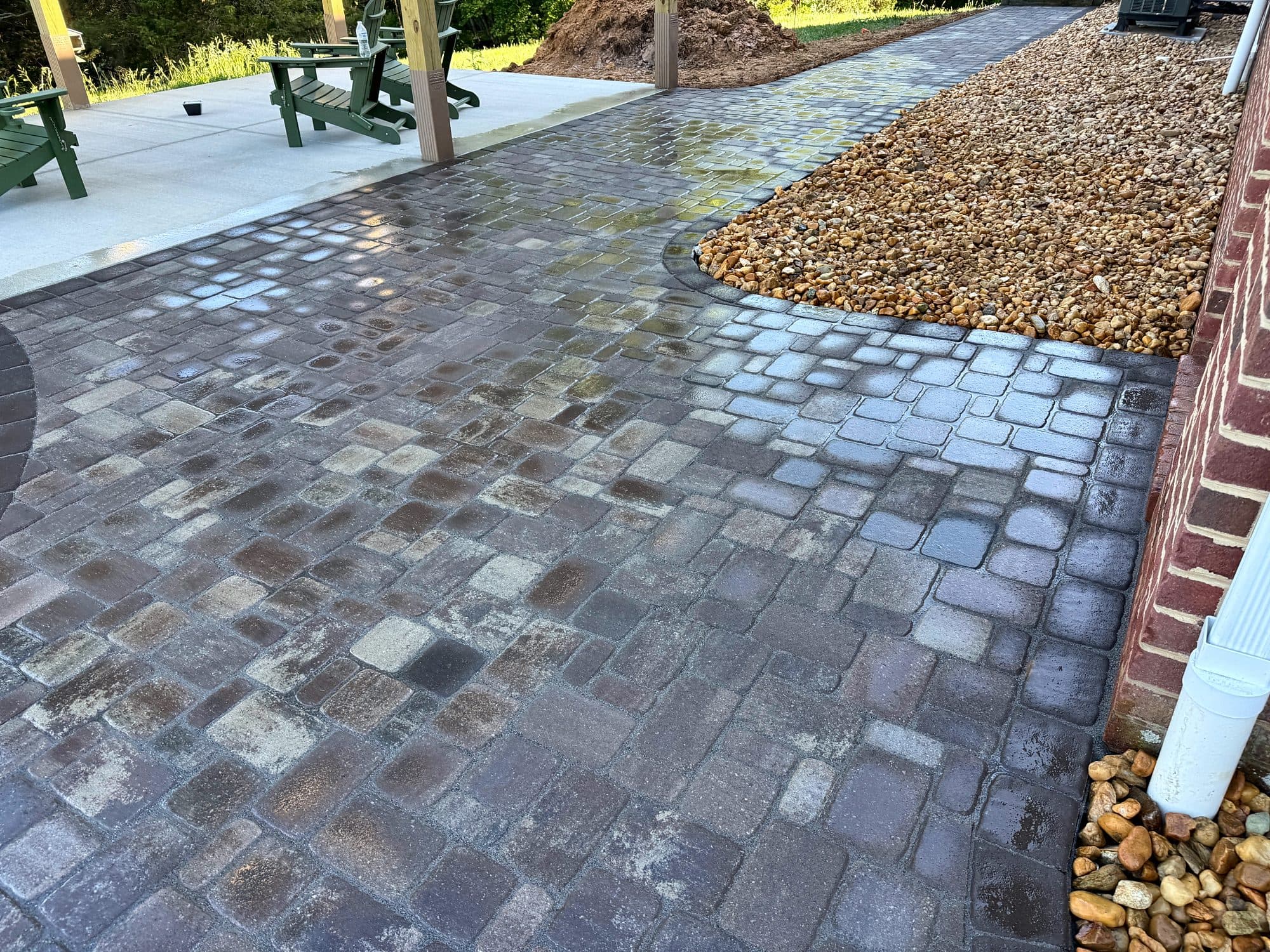Tumbled pavers in blended gray and tan tones meeting a concrete porch slab, with a curved river rock bed.